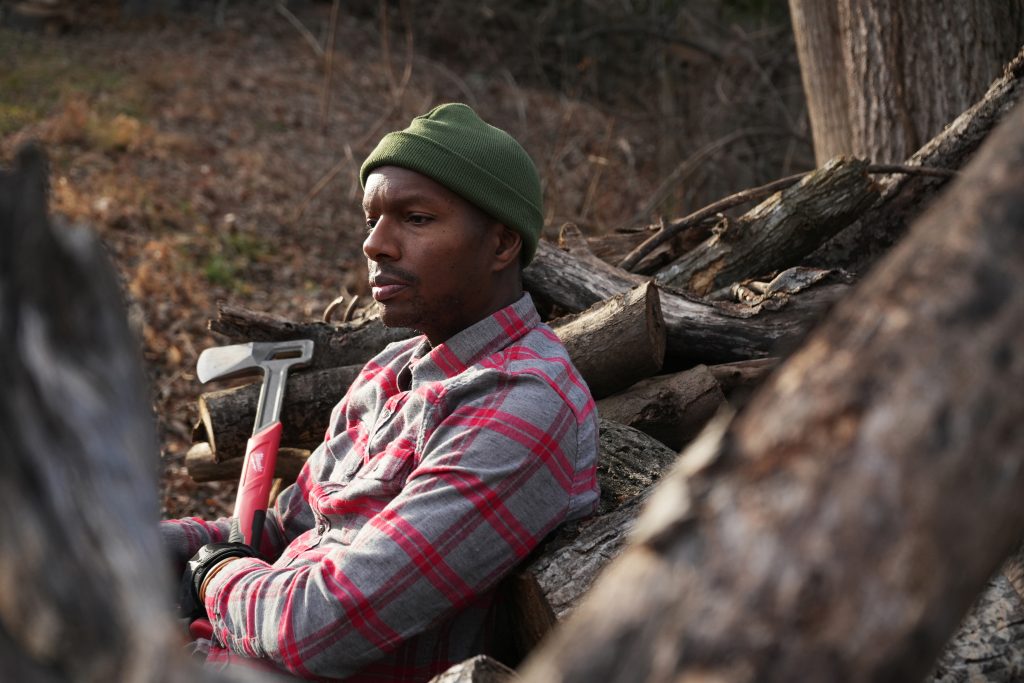 Man resting on wood with an axe, side view
