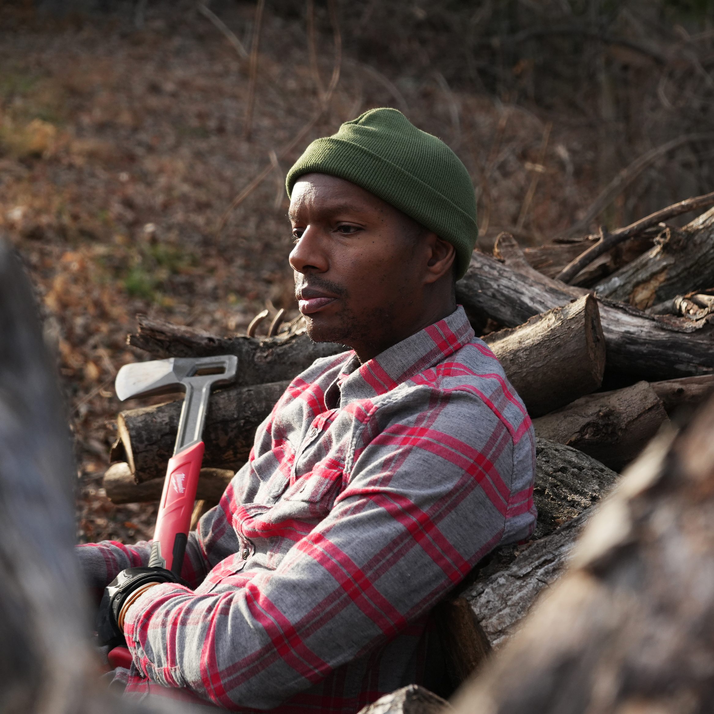 A man with an axe leaning on a pile of wood to be chopped.